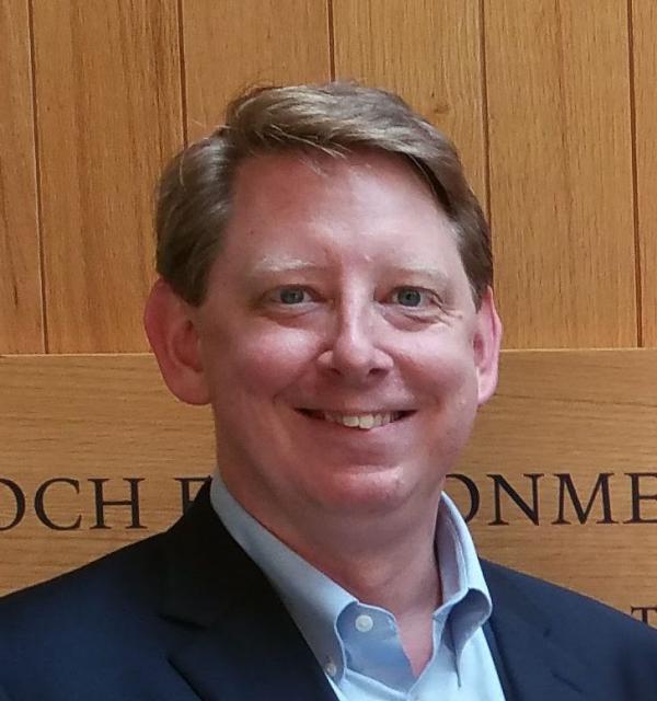 Peter Burke smiling at camera in front of wooden background